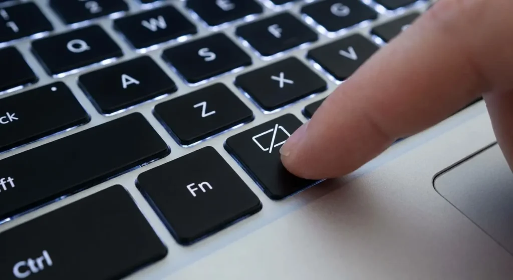 Close-up of a laptop keyboard with a finger pressing the function key (F7) marked with a touchpad icon, next to the Fn key.